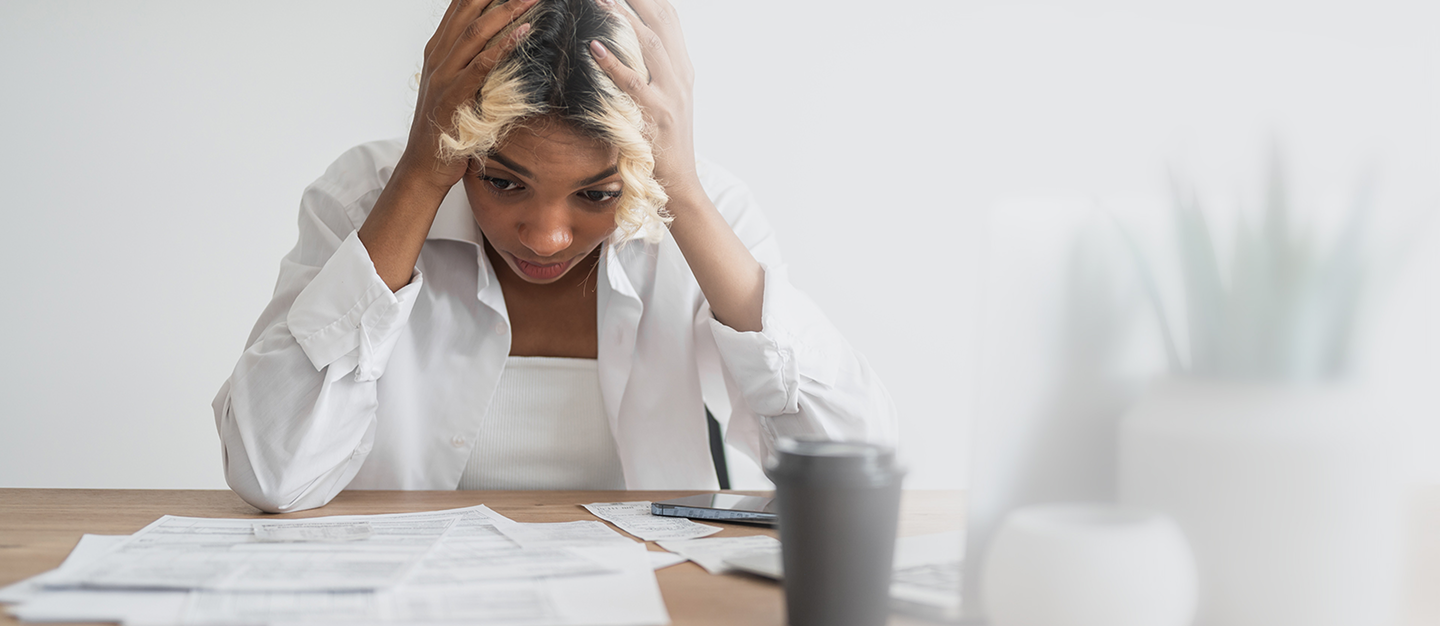 A stressed woman puts her hands on her head as she looks at bills